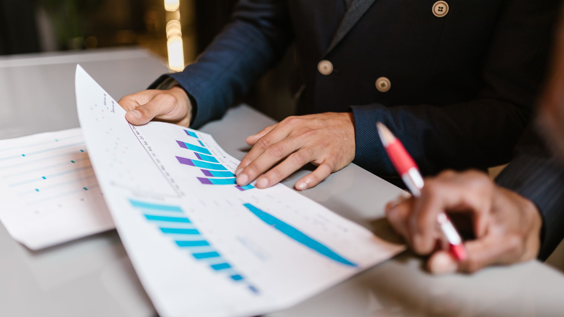 Profissionais analisando gráficos financeiros impressos sobre a mesa durante uma reunião de negócios